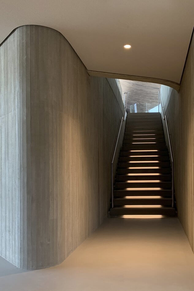 Moderne Treppe mit fugenloser Wandgestaltung und sanfter Beleuchtung im Eingangsbereich.