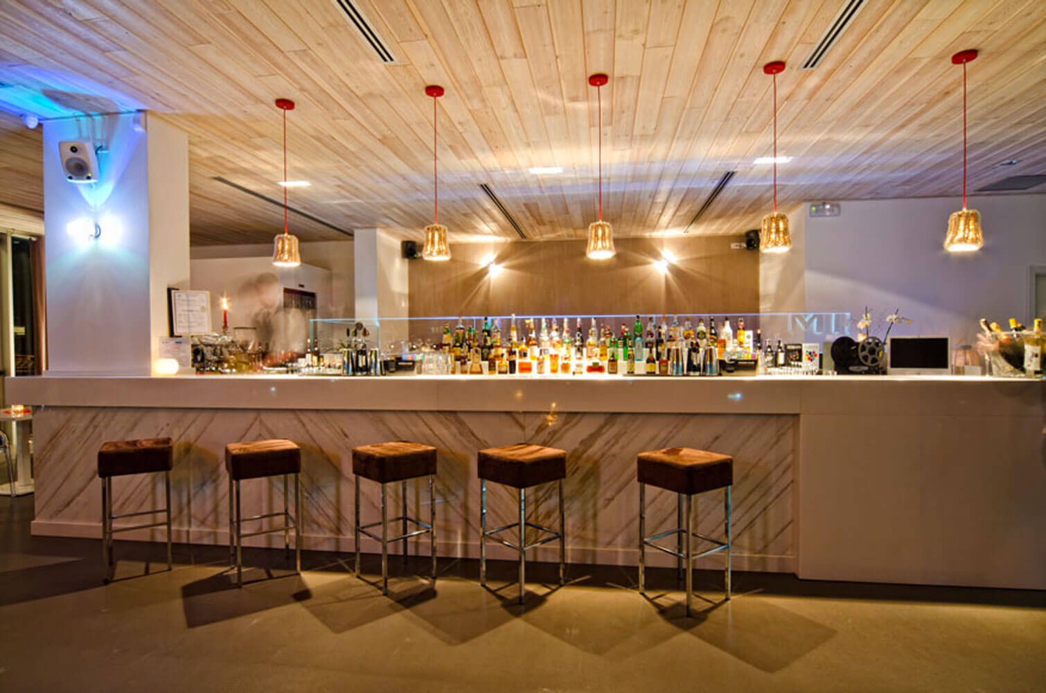 Moderne Bar mit Holzdecke, stilvollen Hockern und vielfältigen Getränken im Hintergrund.